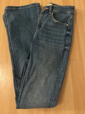 Blå slim fit jeans med fem fickor - Snygga blå bootcut jeans med klassisk femficksdesign. Jeansen har låg midja och stängs med knapp och dragkedja. Perfekta för en avslappnad och trendig look.