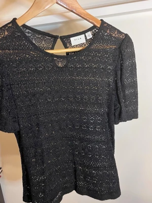Svart spetsblus L - Snygg svart blus från Vila i genombruten spets med korta ärmar och rund halsringning. Passar både dem som har M och L. Använd en gång
