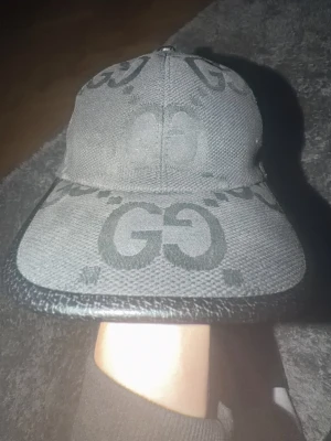 Svart keps från Gucci med GG-mönster - Säljer en svart keps från Gucci med det klassiska GG-mönstret över kepsen. Detta är en Jumbo modell, fint skick inte använd så mkt alls! Box och kasse följer med 