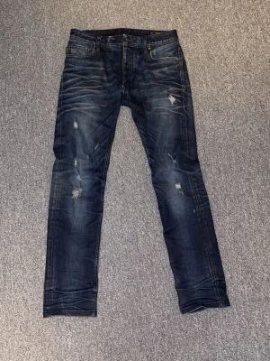 Mörkblå Jeans - Snygga mörkblå jeans från Jack & Jones med slim fit passform + klassiska slitningar. Storlek W29. OBS: Knappen som knäpper ihop jenasen saknas.