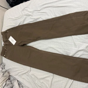 Bruna jeans från Calvin Klein Jeans - Snygga bruna jeans från Calvin Klein Jeans med klassisk femficksdesign och raka ben. Jeansen har silverfärgade nitar och knapp, samt diskret CK-logo på fickan. Perfekta för en stilren och avslappnad look.