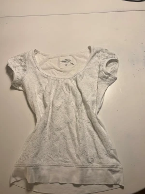 Vit spetsblus från H&M - Söt vit blus från H&M med korta ärmar och rund halsringning. Toppen har ett lager av spets över hela framsidan och är tillverkad i mjuk bomull. Perfekt för dig som gillar romantiska detaljer och enkel stil.
