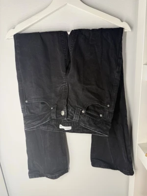 Svarta jeans - Säljer ett par flared svarta jeans från Gina Tricot och klassisk femficksdesign. Jeansen har silverfärgade knappar och detaljer samt en diskret logga på insidan av linningen. Perfekta till en avslappnad och stilren look.