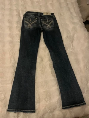 Miss Me Mörkblå low waist bootcut jeans  - Säljer as snygga mörkblå low waist bootcut jeans från Miss Me som tyvärr blivit för små. Byxorna har detaljerade bakfickor med broderi och diamanter. Jeansen har även vita sömmar längs benen. Jeansen är i storlek W23 och är i bra skick. På sista bilden kan man se att det slitits ut lite vid kanten. Frågor eller fler bilder? Kontakta mig💗