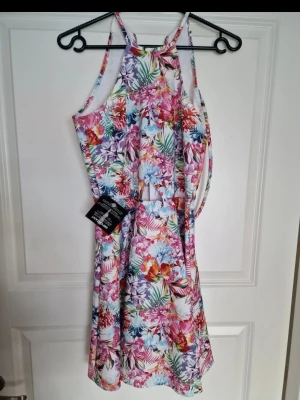 Ny blommig sommarklänning med etikett - Färgglad blommig klänning. Utskurning i midja/mage framsida.