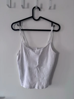 Vit ribbad linnetopp med smala band - Snygg vit ribbad linnetopp med smala axelband och croppad passform. Perfekt till jeans eller kjol för en enkel och fräsch look. Materialet är stretchigt för extra komfort.