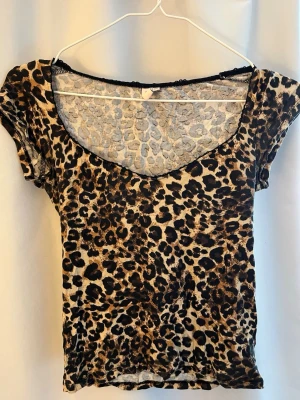 Leopardmönstrad tight topp - Snygg topp med leopardmönster i beige, brunt och svart. Modellen är tight med korta ärmar och djup v-ringning. Materialet känns stretchigt och följsamt. Storlek XS 