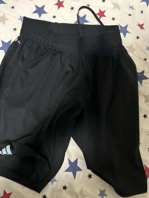 Domare shorts - Svarta träningsshorts från Adidas med elastisk midja och diskret logga på benet. Tillverkade i ett lätt och snabbtorkande material som passar perfekt för sport och aktivitet. Shortsen har en bakficka och klassisk passform.