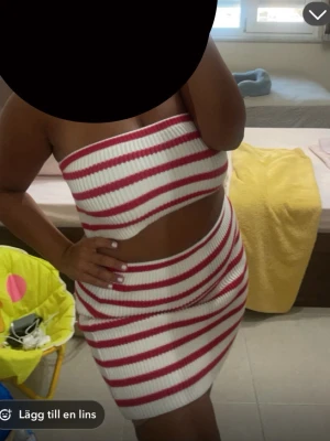 Randig bandeau tubtopp i vitt och rött - Säljer en ribbad bandeau tubtopp med vita och röda ränder. Toppen är ärmlös och croppad, perfekt för varma dagar. Materialet är stretchigt och sitter tight mot kroppen. Snygg att matcha med kjol eller jeans för en trendig look.