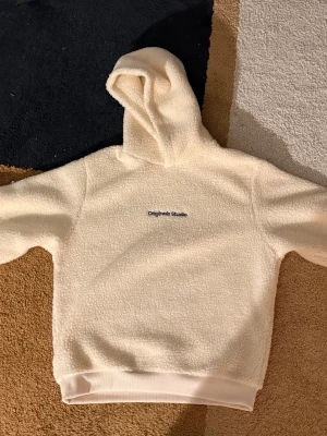 Crèmevit teddy hoodie Jack&Jones - Mysig crèmevit hoodie från Jack&Jones i teddyfleece. Hoodien har broderad logga på bröstet, stor huva och ribbade muddar. Perfekt för dig som gillar en avslappnad och trendig stil med extra komfort.