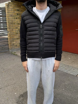 Moncler Cardigan - Snygg svart cardiganjacka med vadderad front och huva. Ärmar och rygg är ribbstickade för en modern look. Jackan har dragkedja framtill, fickor med knapp och en ficka på ärmen. Perfekt för lager-på-lager och streetwear-stil.