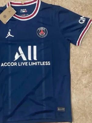 PSG matchtröja blå Jordan x Nike - Snygg blå PSG matchtröja med vita och röda detaljer. Tröjan har klubbmärke på bröstet, Jordan-logga och sponsortryck framtill. Rund halsringning med röd och vit kant. Perfekt för dig som älskar fotboll och vill representera Paris Saint-Germain.