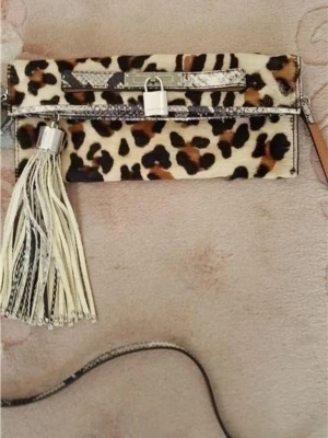 Leopardmönstrad kuvertväska med tofs - Fantastisk fin Karen Millen väska med axelrem, leopardmönstrad. Den är i princip oanvänd i perfekt skick. Den har dragkedja.toffs och en magnet knapp  Det finns en ficka inuti i väskan.  Mått: längd 25 cm. Hög 17 cm. axelband 100 cm.