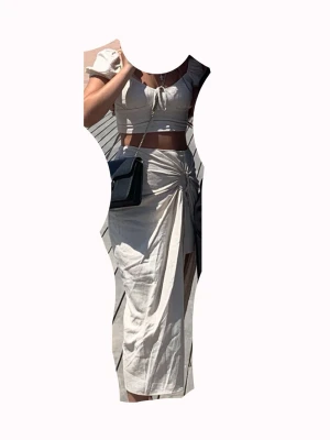 Beige set med puffärm och knyt från stradivarius - Säljer ett beige tvådelat set med crop top och kjol. Toppen har puffärmar och knyt fram, kjolen är midilång med hög slits och knyt i midjan. Setet har en avslappnad och trendig look, perfekt för sommardagar. Materialet ser ut att vara lätt och luftigt. OBS: FRAKTAR INOM 24H!🩷