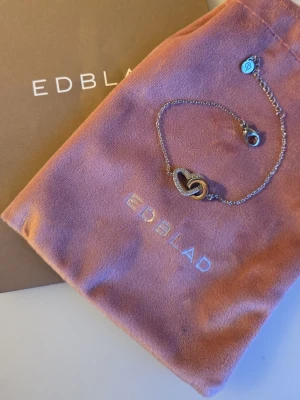 Silverfärgat Eternal Heart armband från Edblad - Snyggt armband i silverfärg från Edblad med ett hjärthänge dekorerat med små gnistrande stenar. Kedjan är tunn och har ett litet Edblad-märke vid låset. Perfekt accessoar för att lyfta din outfit med lite extra bling.