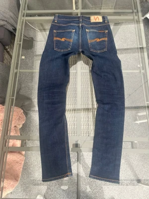 Nudie Jeans Lean Dean – Dry 16 Dips (W28 L32) - Säljer ett par superfina Nudie Jeans i modellen "Lean Dean". Färgen heter "Dry 16 Dips" och är en klassisk, djup indigo som ger en riktigt snygg look. Dessa är tillverkade i 99% ekologisk bomull med 1% elastan, vilket gör att de sitter slimmat men ändå är bekväma att röra sig i. De är i mycket bra skick och redo att få en ny ägare. Perfekt för dig som vill ha ett par hållbara jeans av hög kvalitet. Kort info:  Märke: Nudie Jeans  Modell: Lean Dean  Tvätt: Dry 16 Dips  Storlek: W28 L32 