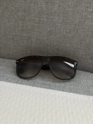 Svarta Ray-Ban pilotbågar solglasögon - Snygga bruna solglasögon från Ray-Ban med klassisk pilotbåge och mörka glas. Bågarna är i plast och har Ray-Ban-loggan på sidan. Perfekta för dig som vill ha en tidlös och cool stil.
