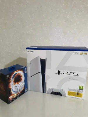 Sony PlayStation 5 med headset - Säljer en PlayStation 5 konsol från Sony i vit och svart design, med 1TB lagring och stöd för 4K HDR. Medföljer ett vitt stereo gaming headset med blå detaljer, justerbart huvudband och mikrofon. Perfekt för gaming och uppslukande spelupplevelser.