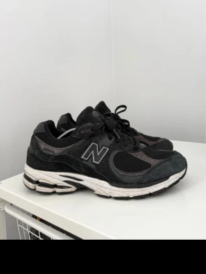 Svarta New Balance 2002R sneakers - Snygga svarta New Balance 2002R sneakers med mesh och mockadetaljer. Skorna har en chunky vit sula och klassisk N-logga på sidan. Perfekta för dig som gillar streetwear och sportig stil.