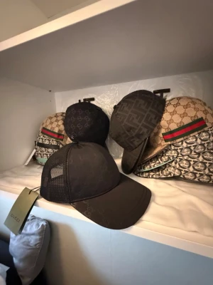 Svart Gucci keps - Snygg svart keps med GG-mönster över hela kepsen och mesh på sidorna för extra ventilation. Klassisk böjd skärm och justerbar rem bak. Perfekt accessoar för en trendig streetwear-look.