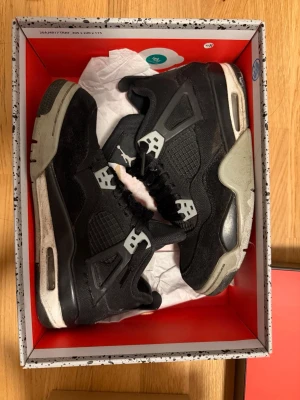 Svarta Air Jordan 4 Retro sneakers - Klassiska Air Jordan 4 Retro sneakers i svart med grå detaljer och vit Jumpman-logga på plösen. Skorna har meshpaneler, mockaliknande material och plastdetaljer vid snörningen. Tjock sula med synlig Air-enhet ger en sportig vibe.