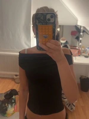 Svart offshoulder topp - Snygg svart offshoulder topp med tight passform. Toppen har en axelbandslös design och sitter snyggt över axlarna. Perfekt att styla med jeans eller kjol för en trendig look.