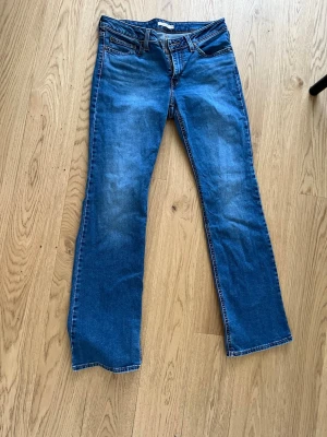 Blå Superlow Bootcut Jeans från Levis - Snygga blå bootcut jeans från Superlow i klassisk denim med låg midja och utsvängda ben. Jeansen har fem fickor, kontrastsömmar och en cool tvättad look. Perfekta för dig som gillar retrovibbar och avslappnad stil.