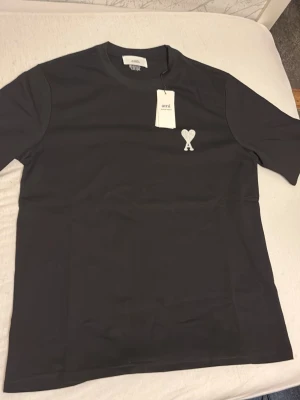 Svart t-shirt från Ami Paris - Snygg svart t-shirt från Ami Paris med klassisk passform och rund hals. På bröstet finns Ami:s ikoniska hjärta med A broderat i vitt. Tillverkad i mjuk bomull som känns skön mot huden. Perfekt till jeans eller shorts.