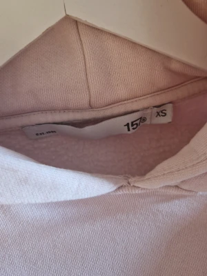 Ljusrosa hoodie från 157  - Ljusrosa hoodie från 157 i storlek XS. Hoodien har en klassisk huva, magficka och ribbade muddar vid ärmar och nederkant. Tillverkad i mjukt material som känns skönt mot huden. Enkel och stilren design som passar till det mesta.
