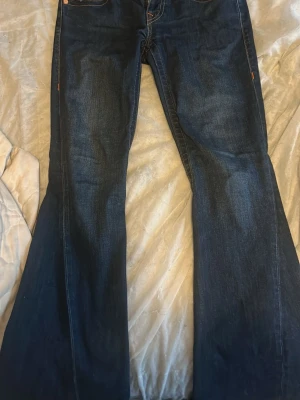 Mörkblå bootcut jeans - Säljer ett par mörkblå bootcut jeans med klassisk femficksdesign och kontrastsömmar. Jeansen har utsvängda ben och är tillverkade i ett slitstarkt denimtyg. Perfekta för dig som gillar retrovibbar och vill ha ett par jeans med snygg passform.