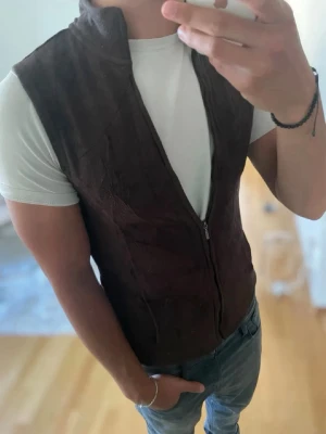 Brun mockaväst från L.L.Bean - Snygg brun mockaväst från L.L.Bean med dragkedja framtill. Västen har en klassisk passform och är perfekt att bära över en t-shirt eller skjorta för en stilren look. Materialet är mjukt och ger en exklusiv känsla. Pris kan diskuteras!