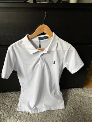 Vit pikétröja från Polo Ralph Lauren som passar S - Klassisk vit pikétröja från Polo Ralph Lauren med korta ärmar och krage. Tröjan är storlek M men passar storlek S! Tröjan är nytt skick och inga skador, pris kan diskuteras. Hör av er vid funderingar!