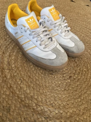 Adidas samba - Fräscha Adidas sneakers i vitt läder med gula detaljer och klassiska tre ränder på sidan. Dom änvända. Men är mest smutsiga! Så det går att tvätta om man vill. Storleken är 44 2/3. Original boxen har jag tyvärr inte kvar. En liten defekt på vänstra skorn.