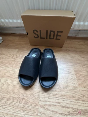 Svarta Yeezy Slide tofflor - Tillverkade i ett mjukt och bekvämt syntetmaterial. Helt oanvända, fråga gärna om fler bilder, priset kan diskuteras.
