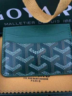 Plånbok grön - Snygg grön korthållare med det klassiska handmålade mönstret i vitt, brunt och svart. Tillverkad i exklusivt läder och canvas, har flera fack för kort och är perfekt för dig som vill ha något både stilrent och lyxigt i fickan.