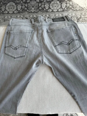 Grå jeans från Replay - Snygga grå jeans från Replay med klassisk femficksdesign och raka ben. Jeansen har dekorativa sömmar på bakfickorna och svarta Replay-loggor på både fram- och baksidan. Tillverkade i ett mjukt denimtyg som ger en skön känsla.