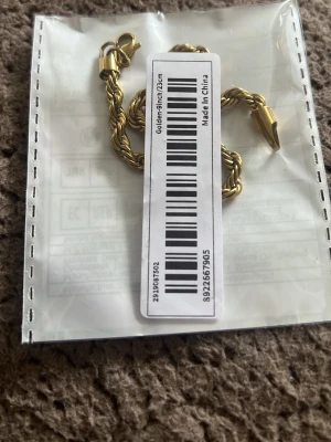 Guldfärgat tvinnat armband - Snyggt guldfärgat armband med tvinnad kedja och karbinlås. Armbandet har en stilren och modern look som passar till många olika outfits. Materialet är metall och längden är cirka 23 cm