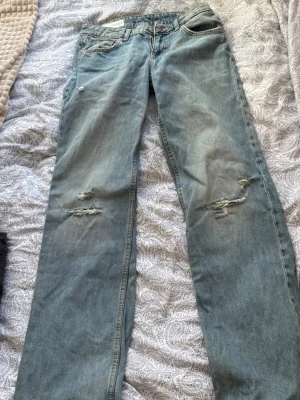 Zara baggy jeans med hål  - Säljer ett par ljusblå jeans med raka ben och flera slitningar framtill och baktill. Jeansen har klassisk femficksmodell och är gjorda i denim. Perfekta för en avslappnad och trendig look.