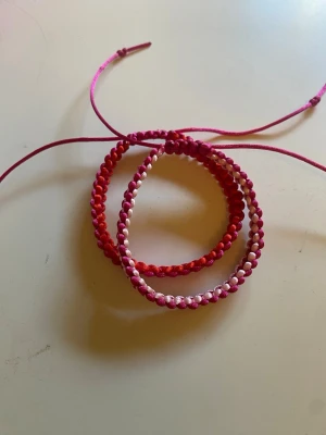 Två handgjorda armband - Säljer två handgjorda armband i makramé med rosa, röda och vita toner. Armbandet har en justerbar knytning så att den ska passa alla! Perfekt accessoar för dig som gillar färg och unika detaljer. Säljer både för 60kr!