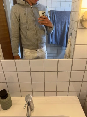 Grå hoodie med dragkedja - Säljer en klassisk grå hoodie från Puma med dragkedja framtill och två stora fickor. Hoodien har justerbar huva med snören och ribbade muddar vid ärmar och midja. Perfekt för en chill och avslappnad stil.
