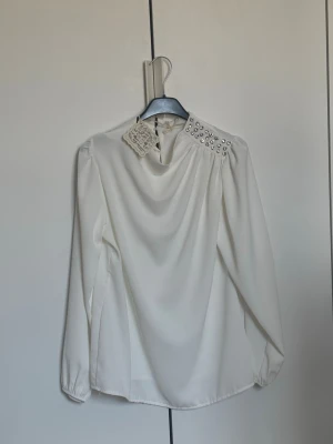 Vit blus med pärldetaljer - HELT NY MED PRISLAPP, KÖPT FÖR 300 Stilren vit blus med långa ärmar och snygga pärldetaljer på ena axeln. Blusen har en lös passform och lätt drapering framtill. Perfekt för dig som gillar en elegant men enkel look. Materialet känns mjukt och följsamt.