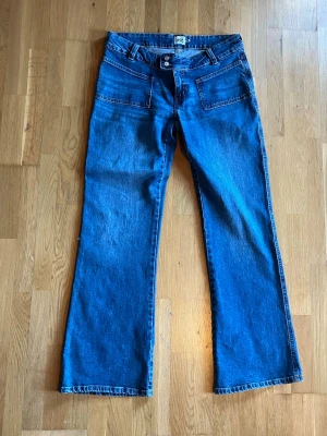 Blå bootcut jeans från Lee - Säljer ett par klassiska blå bootcut jeans från Lee med hög midja och raka ben. Jeansen har två framfickor, två bakfickor och stängs med knapp och dragkedja. Tillverkade i slitstark denim, perfekta för en avslappnad och trendig look.Aldrig använda!