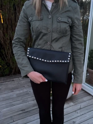 Datorfodral med silvernitar - Stilrent datorfodral tillverkat av veganskt läder i vattentätt material. Fodralet stängs med knapp. Fodralet skyddar din dator effektivt samtidigt som det ger din outfit en extra touch. ⚜️ Storlek: 34 × 25 cm –  Innifrån 33 x 24 📦  