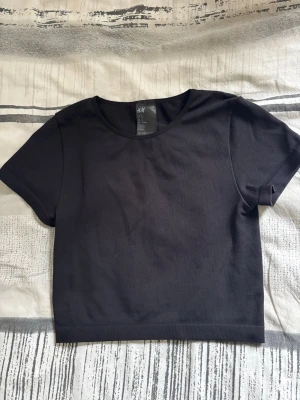 Svart croppad topp från H&M - En svart basic Tshirt från H&M med rund halsringning. Enkel och stilren design som passar perfekt till jeans eller kjol. Tillverkad i mjukt material för en bekväm känsla.