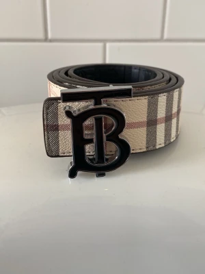 rutigt bälte - Snyggt rutigt bälte med ett B märke på. Mycket klassisk och passar till många outfits. 