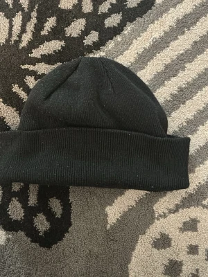 Svart ribbstickad mössa - En klassisk svart ribbstickad mössa med uppvikt kant. Perfekt för att hålla värmen och passar till de flesta stilar. Enkel och stilren design utan synligt märke.