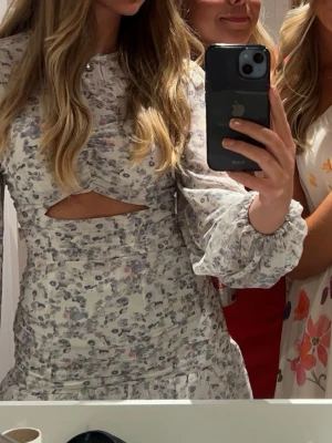 Blommig kortklänning med cut-out - Supersöt kortklänning med blommigt mönster i ljusa toner. Klänningen har långa puffärmar, en liten cut-out under bysten och volang nertill. Perfekt för sommarens alla tillfällen! Endast använd vid 1 tillfälle. 