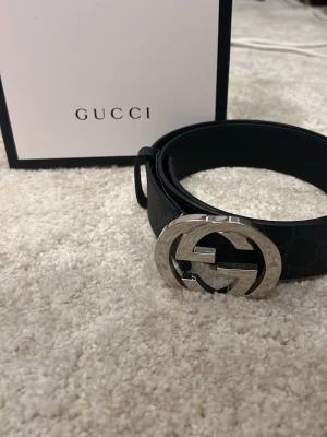 Svart Gucci skärp med silverdetalj - My pris 5200 Snyggt svart skärp från Gucci med klassiskt GG-spänne i silverfärgad metall. Skärpet är gjort i skinn och har diskret mönster längs bandet. Perfekt accessoar för att lyfta din outfit.