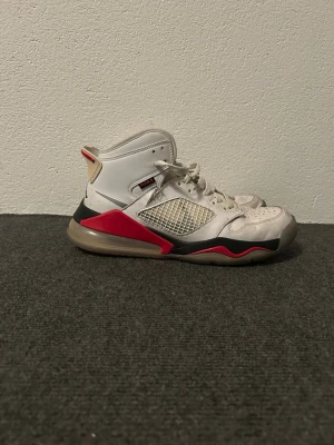 Vita Jordan sneakers med röda detaljer - Snygga vita Jordan sneakers med röda och svarta detaljer. Skorna har meshpaneler på sidorna, högt skaft och klassisk snörning. Sulan är genomskinlig med svarta och röda inslag. Perfekta för dig som gillar streetwear och sportig stil.