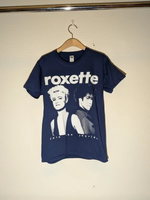 Blå Roxette t-shirt från Fruit of the Loom storlek: Smsl - blå t-shirt med Roxette-tryck framtill från Fruit of the Loom. Klassisk rund hals och korta ärmar. Perfekt för dig som gillar bandtröjor och vill sticka ut med en ikonisk design. Storlek Smal